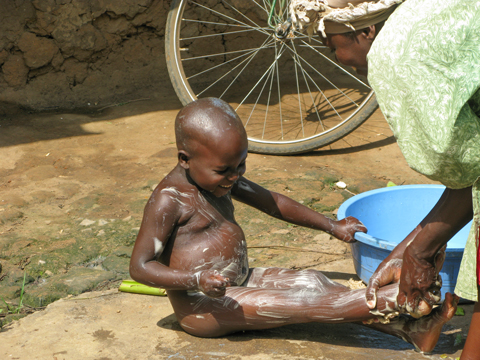 Laughing Ugandan child being bathed outdoors